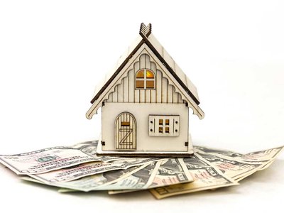 Small wooden toy house on a fanned out bills